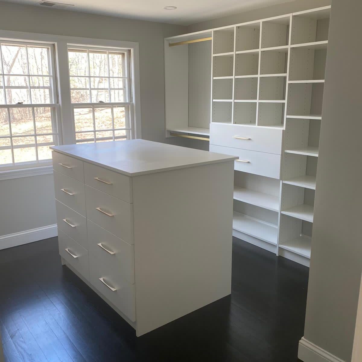 White walk-in closet with drawer island, cubby shelving and brass hang rods