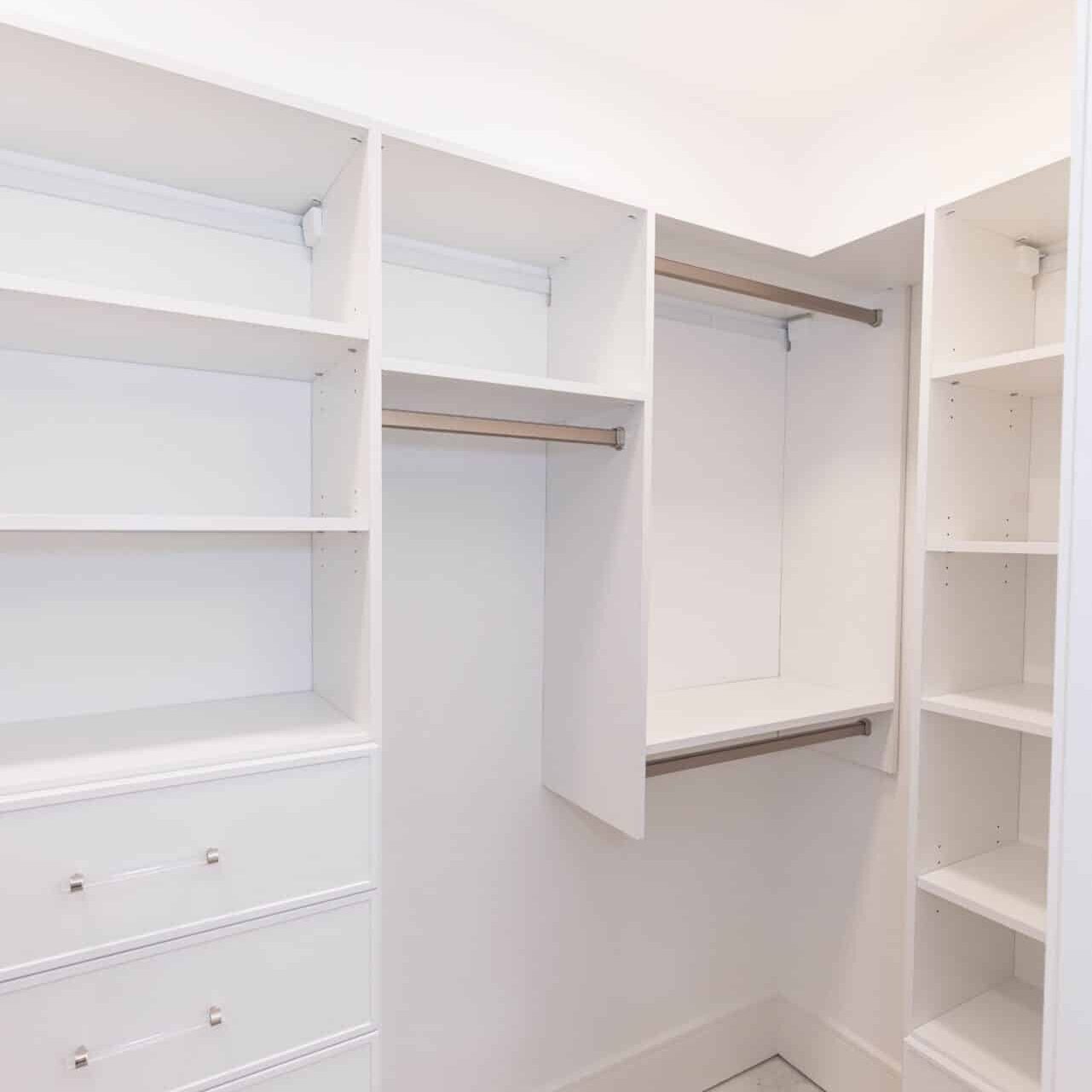 White corner walk-in closet with double hang rods, shelving and drawer bank